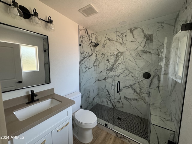 bathroom with vanity, wood-type flooring, a textured ceiling, a shower with shower door, and toilet