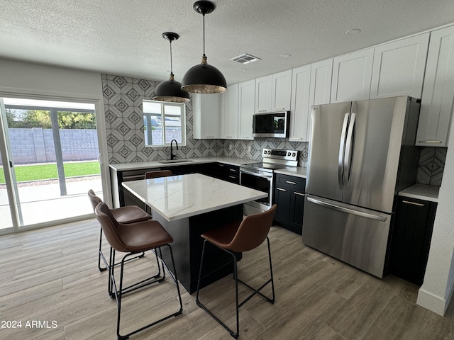 kitchen with pendant lighting, sink, a kitchen island, stainless steel appliances, and a kitchen bar