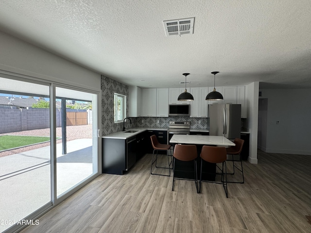 kitchen with pendant lighting, sink, a kitchen island, stainless steel appliances, and light hardwood / wood-style floors