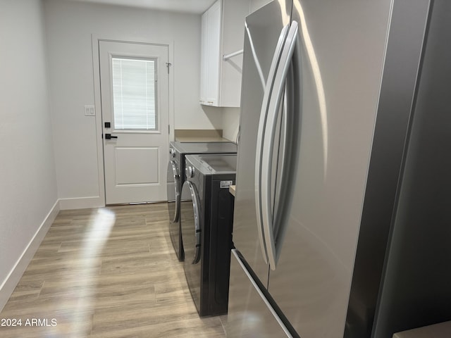 clothes washing area with washing machine and dryer, light hardwood / wood-style floors, and cabinets