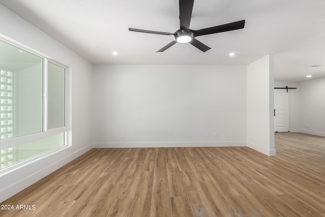 empty room with ceiling fan, light wood-type flooring, and a barn door