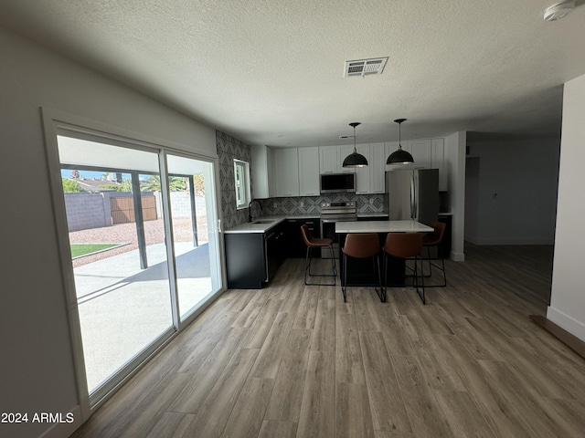 kitchen with a kitchen breakfast bar, pendant lighting, stainless steel appliances, light wood-type flooring, and a center island