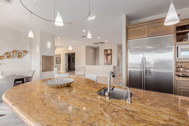 kitchen with sink, light stone counters, built in appliances, pendant lighting, and ornamental molding