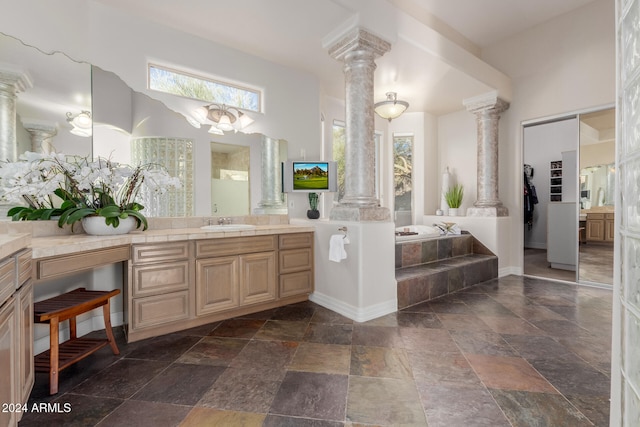 bathroom with a towering ceiling, vanity, decorative columns, and tiled tub