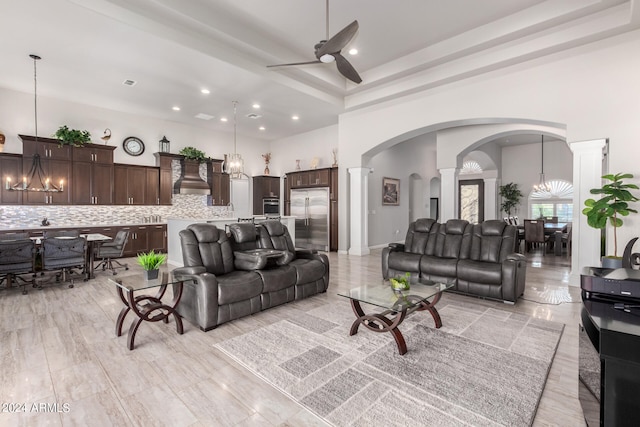 living room with a high ceiling, ornate columns, and ceiling fan with notable chandelier