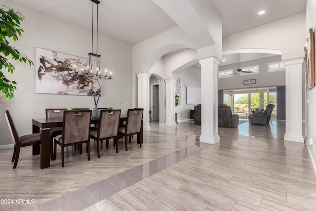 dining space featuring a towering ceiling, a chandelier, ornate columns, and light hardwood / wood-style floors