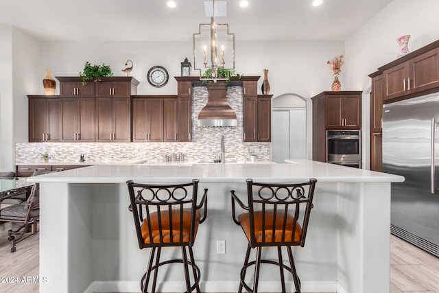 kitchen featuring premium range hood, stainless steel appliances, light wood-type flooring, and backsplash