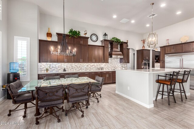 kitchen featuring wall chimney range hood, a breakfast bar area, hanging light fixtures, a center island with sink, and a chandelier