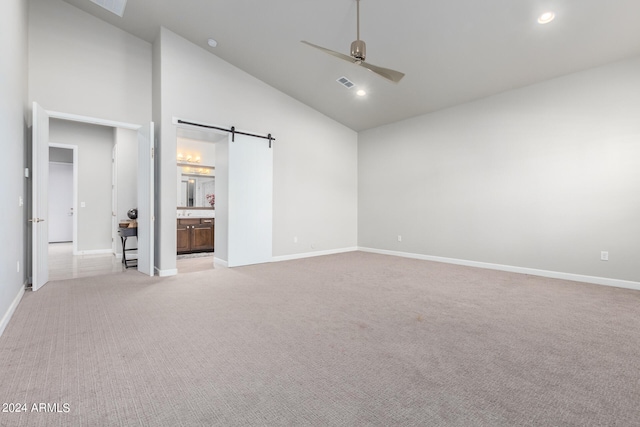 interior space featuring light colored carpet, ensuite bathroom, high vaulted ceiling, and a barn door