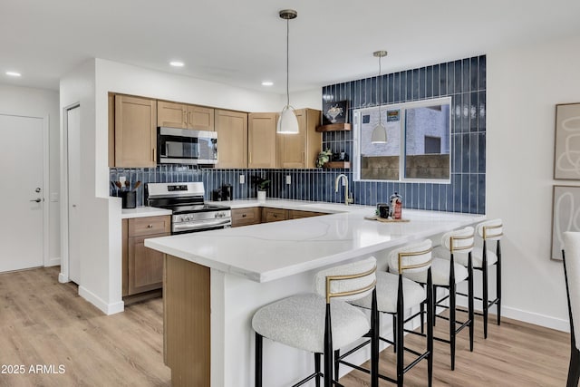 5122 W Mercury Way, Chandler, AZ 85226 - kitchen featuring stainless steel appliances, a peninsula, light wood-style floors, tasteful backsplash, and a kitchen bar