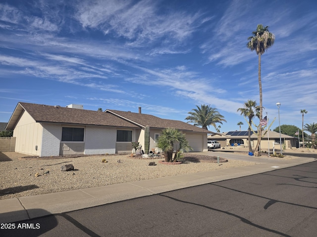 ranch-style house featuring driveway, brick siding, roof with shingles, and an attached garage