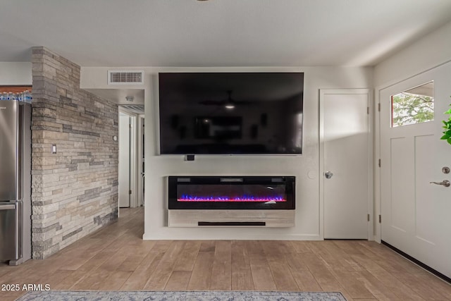 unfurnished living room featuring wood finished floors, a glass covered fireplace, and visible vents