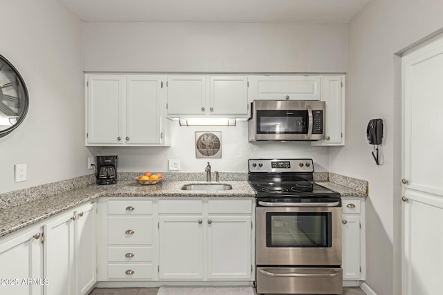 kitchen with white cabinets, light stone counters, stainless steel appliances, and a sink