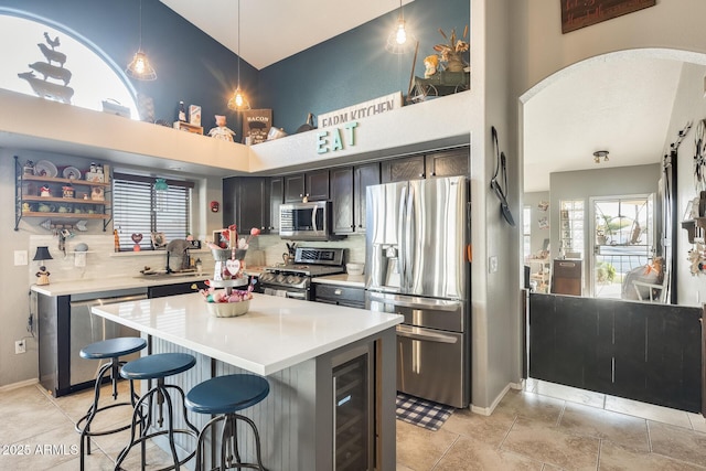 kitchen with sink, hanging light fixtures, stainless steel appliances, a center island, and beverage cooler