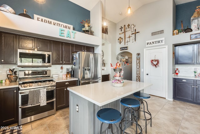 kitchen with dark brown cabinetry, a breakfast bar area, decorative light fixtures, a kitchen island, and stainless steel appliances