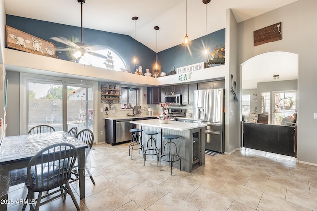 kitchen with a breakfast bar area, a kitchen island, ceiling fan, stainless steel appliances, and decorative backsplash