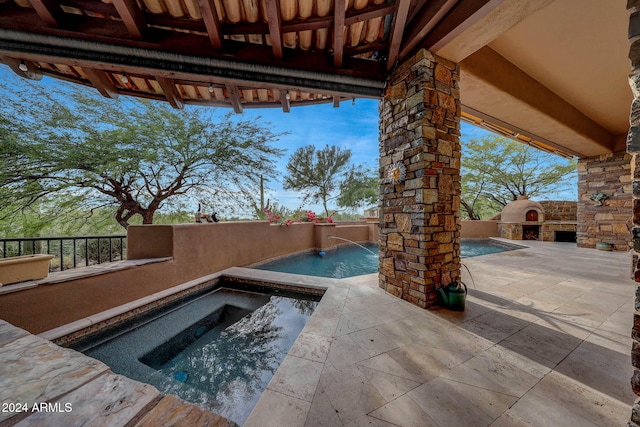 view of swimming pool with a patio area, an outdoor stone fireplace, pool water feature, and an in ground hot tub