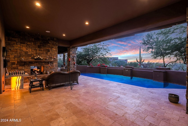 patio terrace at dusk featuring exterior kitchen and an outdoor stone fireplace