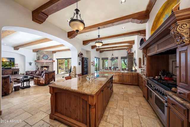 kitchen with a stone fireplace, double oven range, a center island, beamed ceiling, and decorative light fixtures