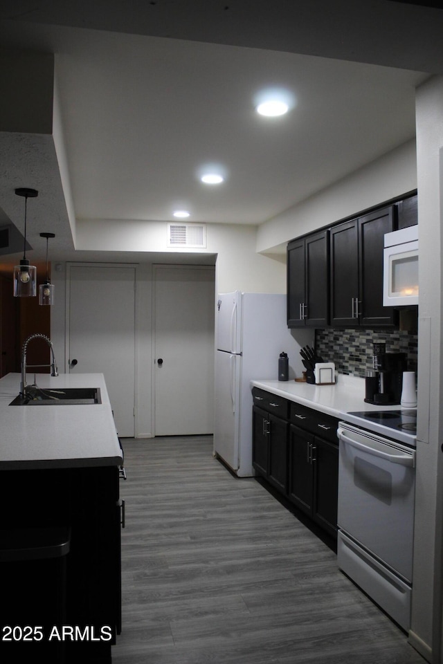 kitchen featuring dark wood finished floors, tasteful backsplash, light countertops, a sink, and white appliances