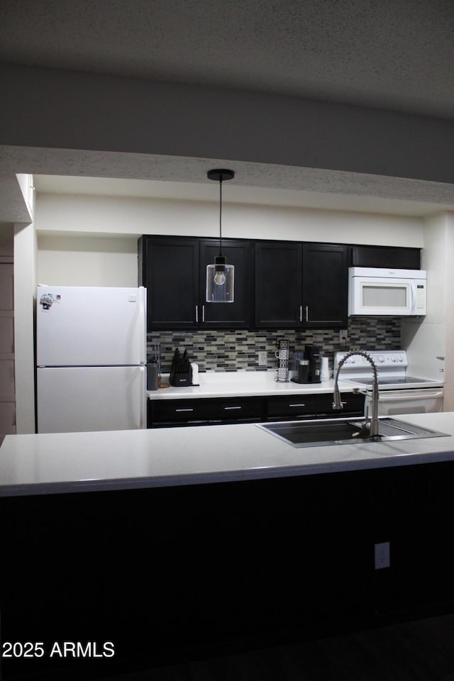 kitchen featuring white appliances, decorative light fixtures, light countertops, dark cabinetry, and backsplash