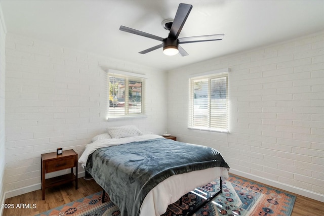 bedroom featuring ceiling fan, brick wall, and dark hardwood / wood-style flooring