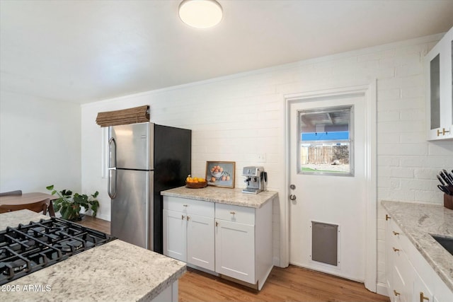 kitchen with stainless steel fridge, white cabinetry, light stone counters, gas stovetop, and light hardwood / wood-style floors