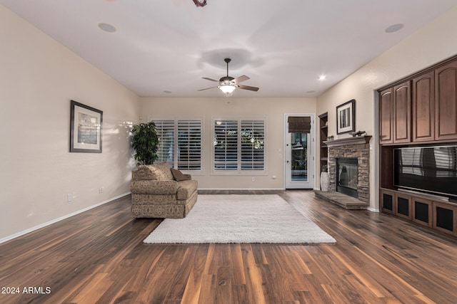 living room featuring a stone fireplace, ceiling fan, and dark wood-type flooring