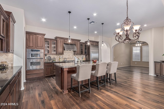 kitchen featuring a kitchen island with sink, ceiling fan with notable chandelier, hanging light fixtures, dark hardwood / wood-style flooring, and stainless steel appliances