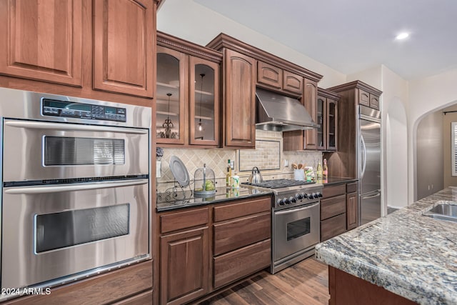 kitchen with dark hardwood / wood-style flooring, ventilation hood, dark stone counters, and high quality appliances