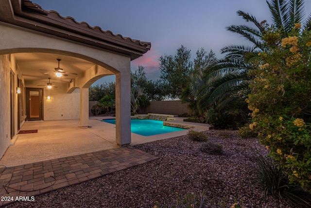 pool at dusk with a patio area and ceiling fan