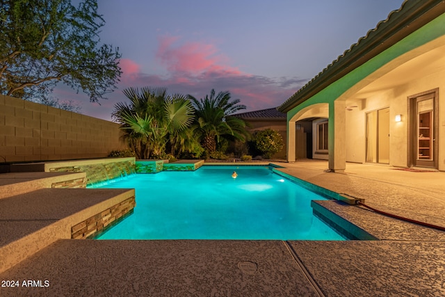 pool at dusk featuring pool water feature and a patio