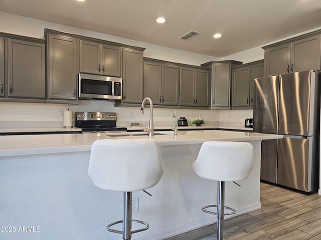 kitchen with visible vents, a kitchen breakfast bar, stainless steel appliances, light countertops, and a sink