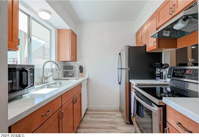 kitchen with appliances with stainless steel finishes, under cabinet range hood, a sink, light countertops, and light wood-type flooring