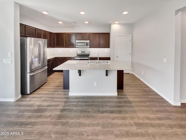 21081 W Almeria Rd, Buckeye, AZ 85396 - kitchen with light stone counters, a sink, a kitchen island with sink, dark brown cabinetry, and appliances with stainless steel finishes