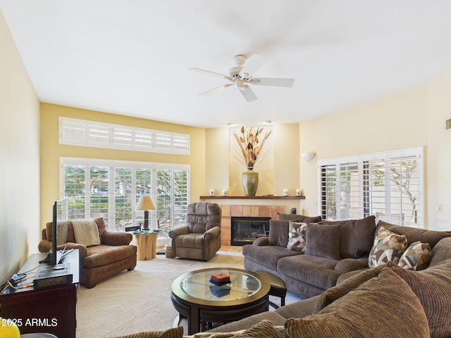 carpeted living area with a tiled fireplace and a ceiling fan