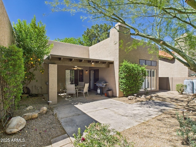 rear view of house with a chimney, stucco siding, fence, and a patio