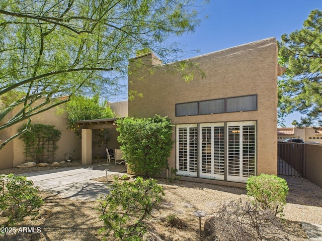 rear view of property featuring stucco siding, fence, and a patio area