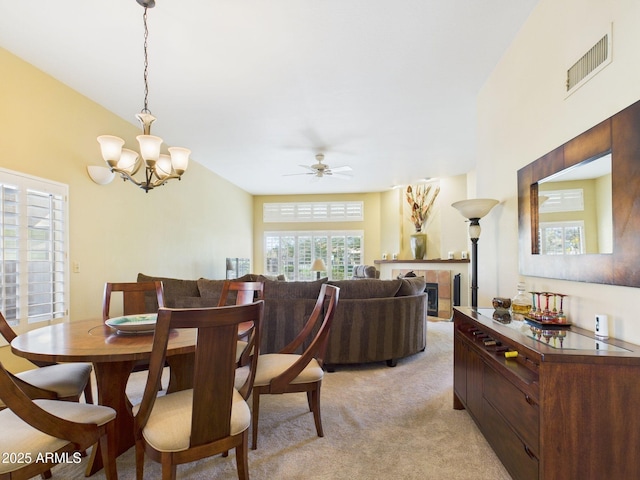 dining space with visible vents, a tiled fireplace, ceiling fan with notable chandelier, and light colored carpet