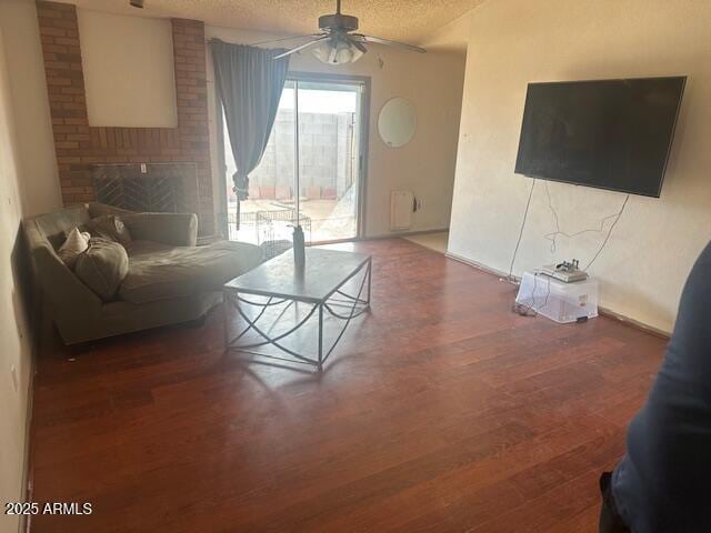 living area with a textured ceiling, a brick fireplace, wood finished floors, and ceiling fan