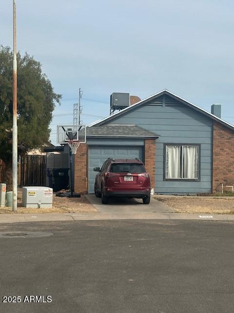 view of front of house with brick siding, fence, central AC unit, a garage, and driveway