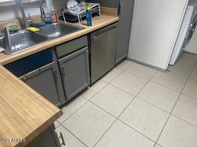 kitchen featuring light tile patterned floors, gray cabinetry, a sink, light countertops, and dishwasher