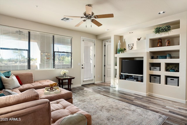 living room with built in features, visible vents, baseboards, and wood finished floors