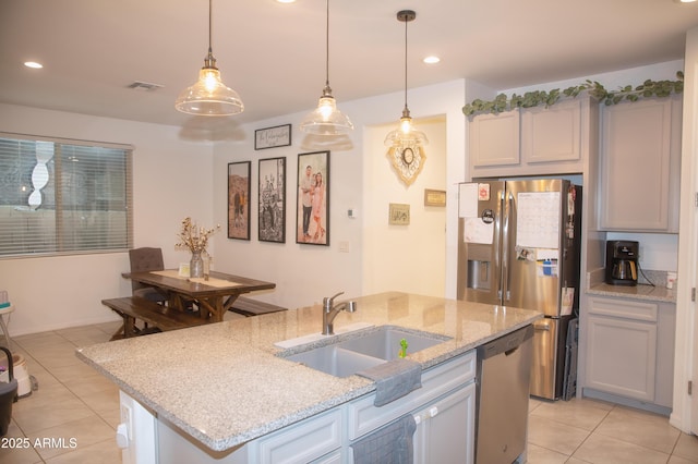 kitchen with a kitchen island with sink, light tile patterned floors, sink, pendant lighting, and stainless steel appliances