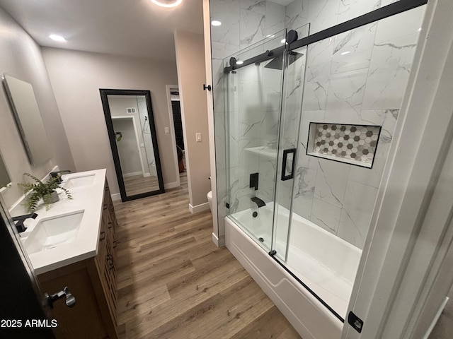 bathroom featuring double vanity, toilet, wood finished floors, combined bath / shower with glass door, and a sink