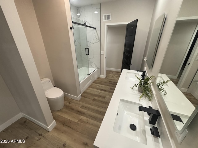 full bathroom with a marble finish shower, visible vents, toilet, wood finished floors, and a sink