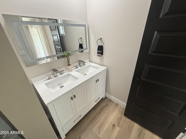 full bath with double vanity, wood finished floors, a sink, and baseboards