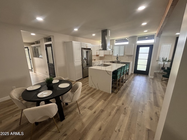 kitchen with stainless steel fridge with ice dispenser, light wood-type flooring, backsplash, and island range hood