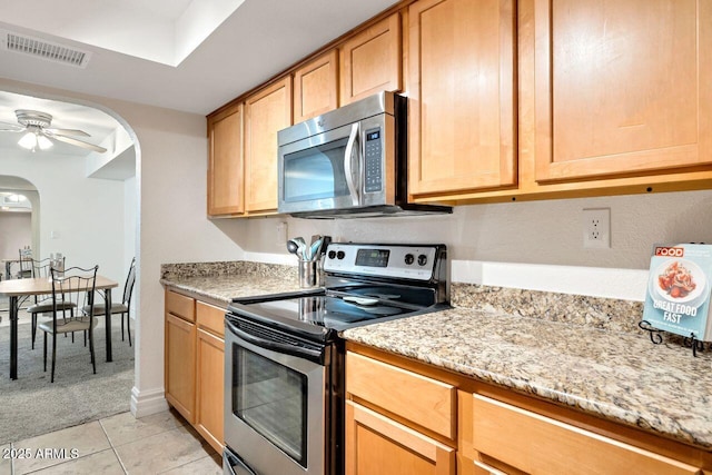 kitchen featuring ceiling fan, appliances with stainless steel finishes, light tile patterned floors, and light stone counters