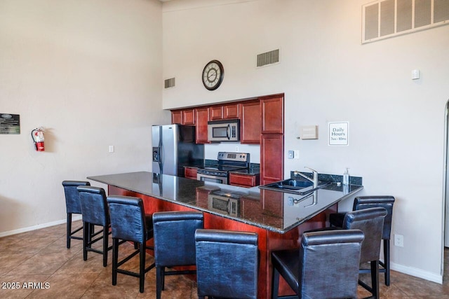 kitchen with appliances with stainless steel finishes, a towering ceiling, sink, a kitchen breakfast bar, and dark tile patterned floors